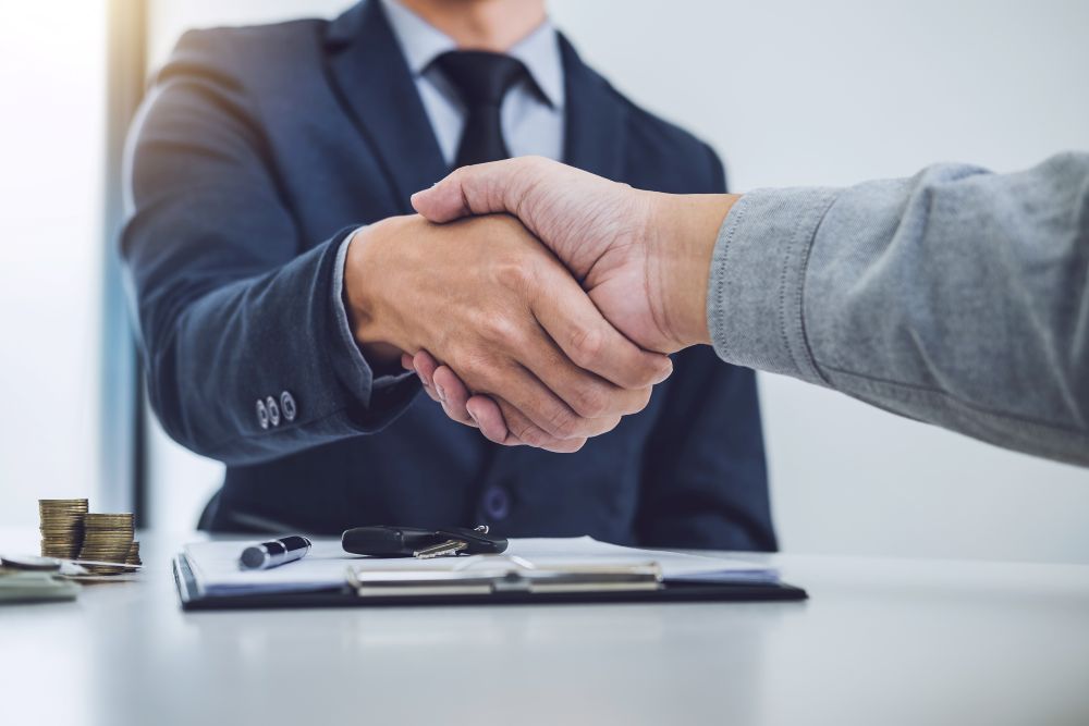 Two men shaking hands with pile of coins in the corner.